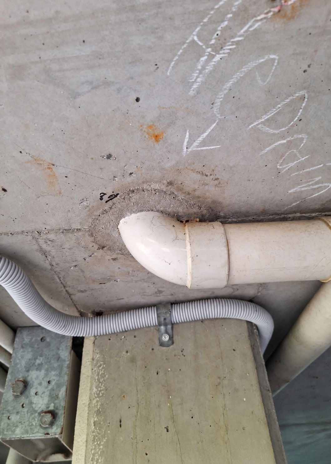 A 100 mm PVC-U elbow immediately below a core-drilled concrete slab before a fire collar is installed