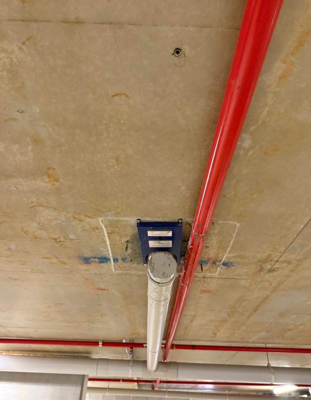 Fendix fire collar installed on a 100 mm PVC-U stack beside a red sprinkler pipe with limited side clearance