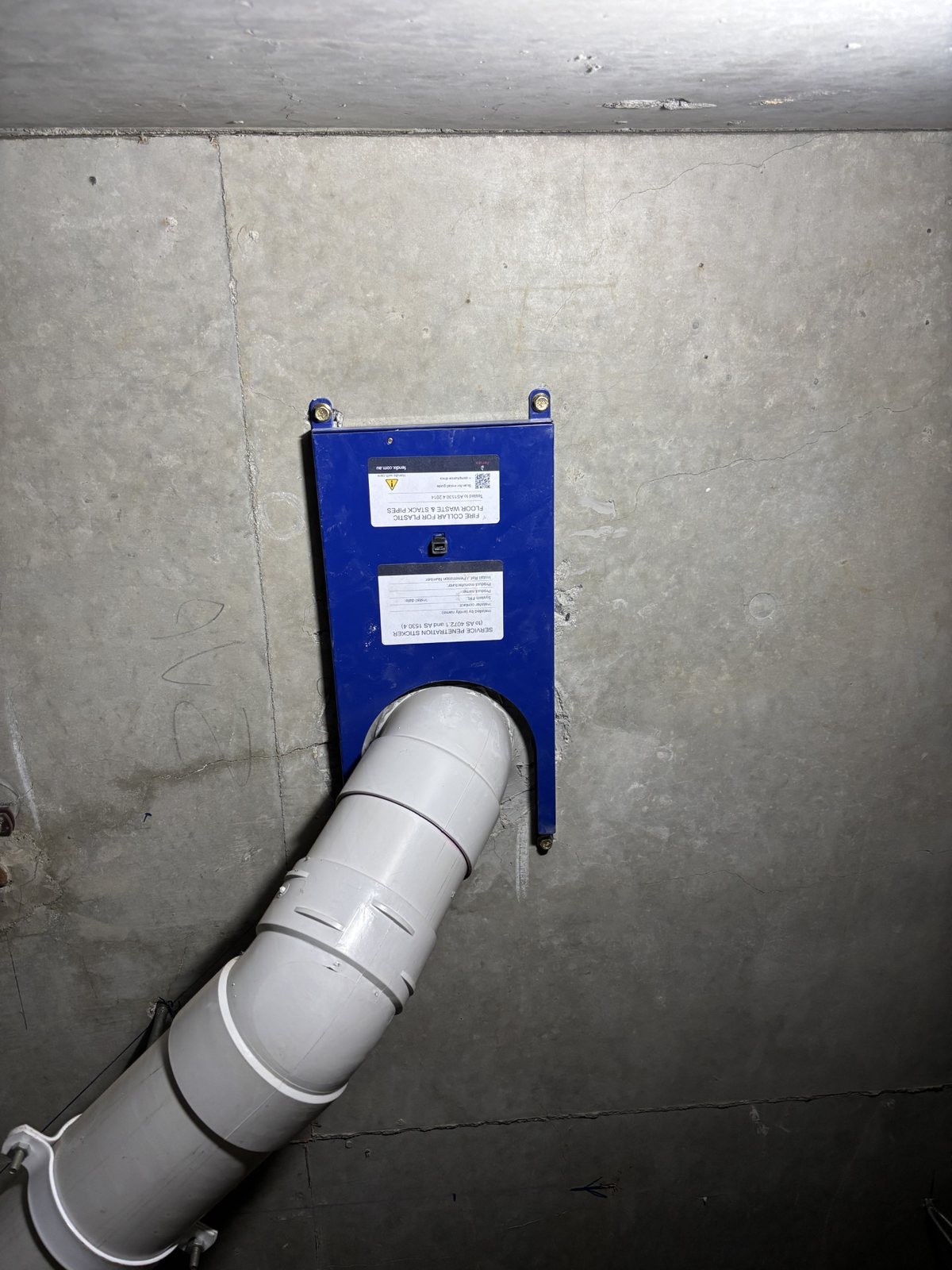 Fendix fire collar installed around a 100 mm PVC-U stack with an elbow directly below the concrete slab