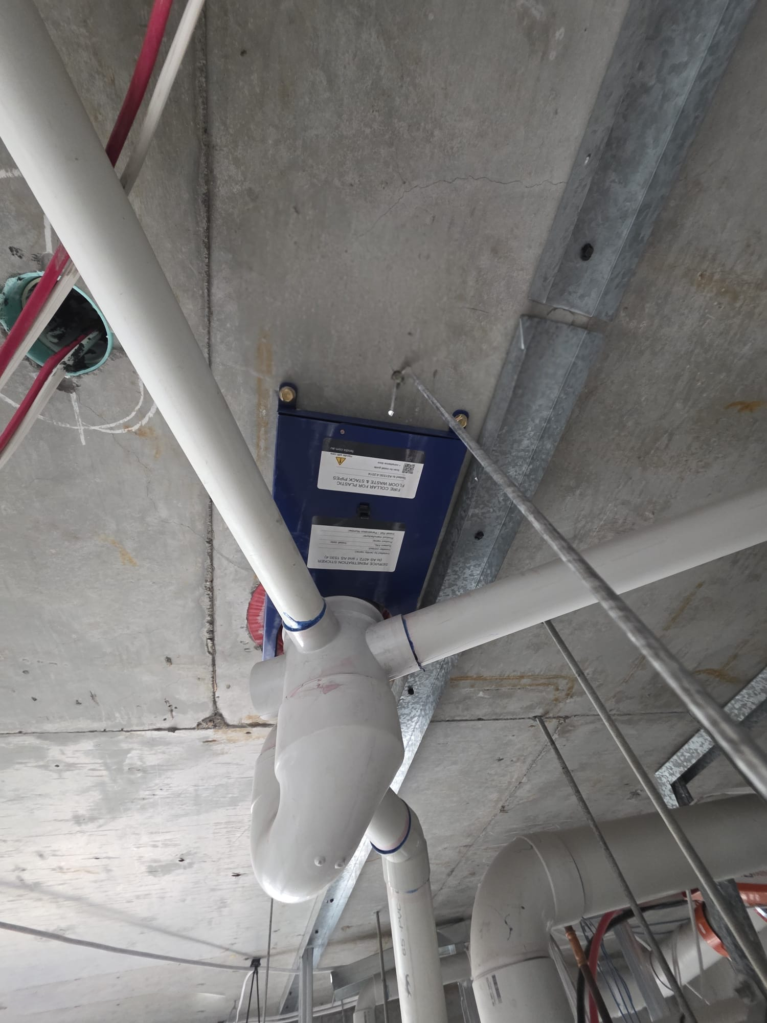 Fendix collar beneath a concrete slab with surrounding pipework and adjacent metal C-track